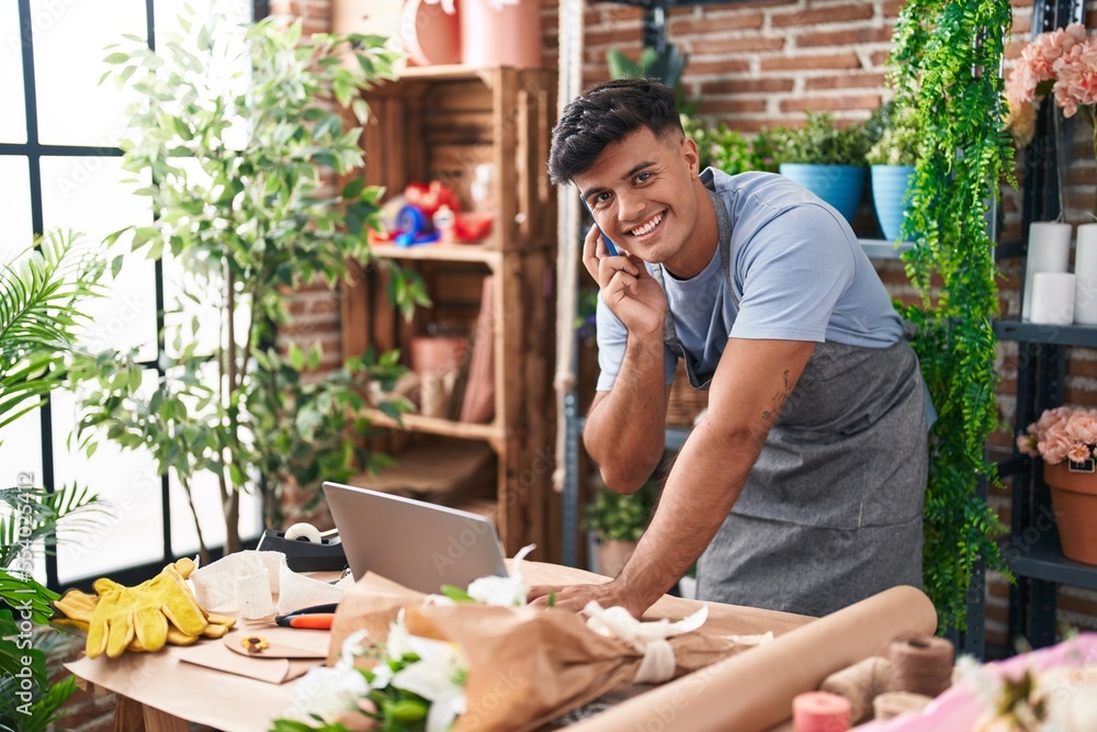 Young hispanic man florist talking on smartphone using laptop at flower shop Young hispanic man florist talking on smartphone using laptop at flower shop