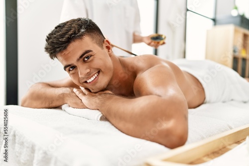 Young hispanic man smiling confident having skin back treatment at beauty center