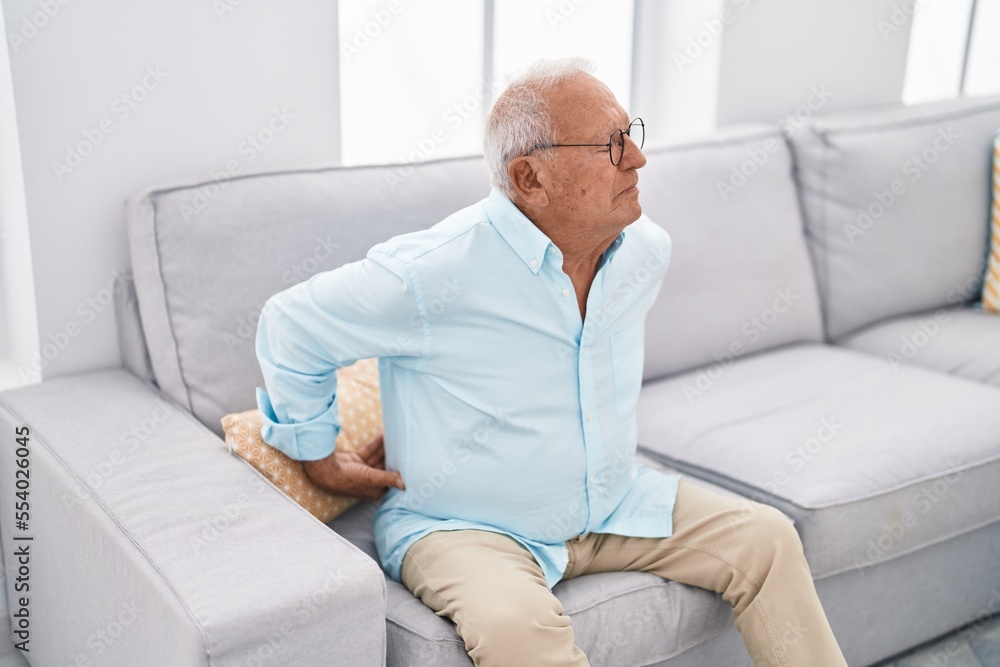 Senior grey-haired man suffering for backache sitting on sofa at home