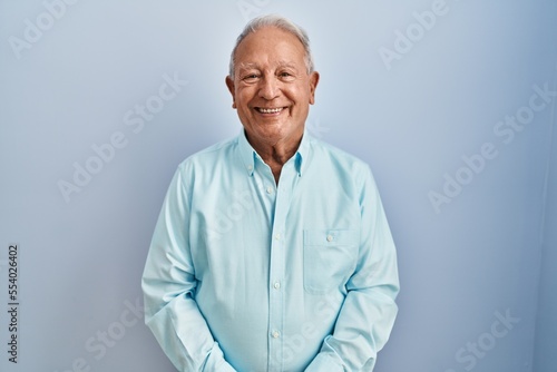 Senior man with grey hair standing over blue background with a happy and cool smile on face. lucky person. © Krakenimages.com