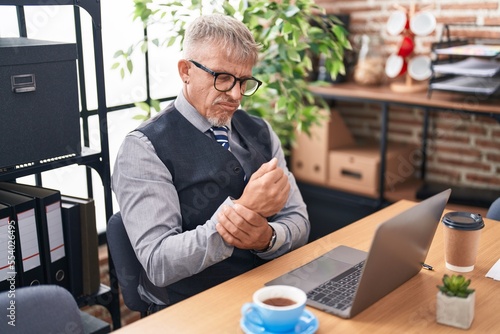 Middle age grey-haired man business worker suffering for wrist pain working at office