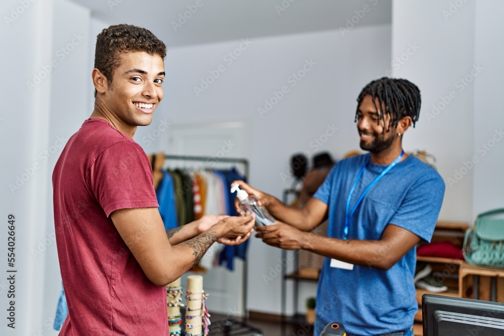 Two men shopkeeper and customer cleaning hands using sanitizer gel at clothing store Two men shopkeeper and customer cleaning hands using sanitizer gel at clothing store