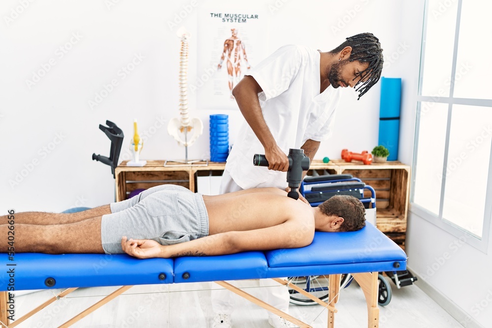 Two men physiptherapist and patient massaging back using percussion pistol at clinic Two men physiptherapist and patient massaging back using percussion pistol at clinic