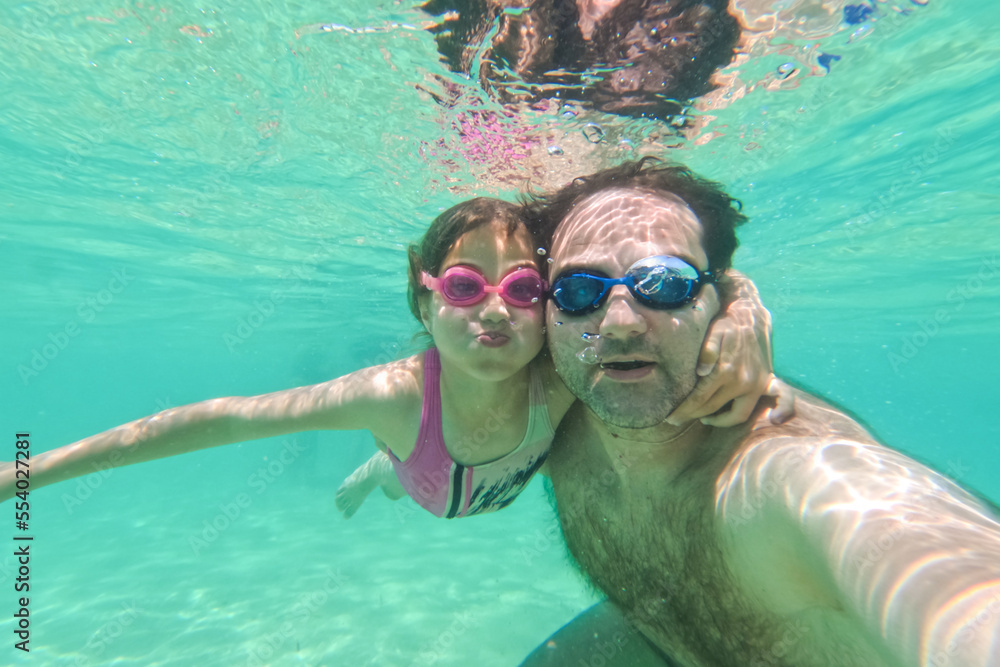 Happy fun underwater portrait of father and daughter with swimming goggles. Summer vacation.