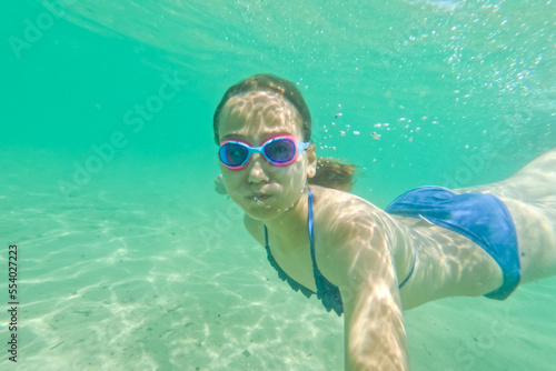 Child girl swimming underwater with swim goggles. Dive and swimming in the sea. Have fun on summer vacation. 