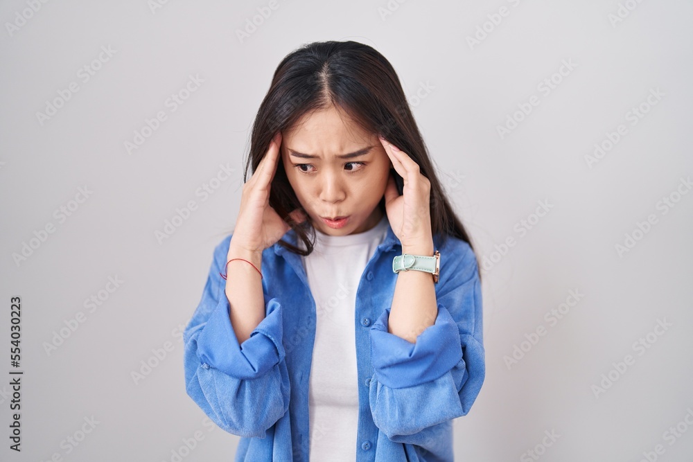 Young chinese woman standing over white background with hand on head, headache because stress. suffering migraine. Young chinese woman standing over white background with hand on head, headache because stress. suffering migraine.