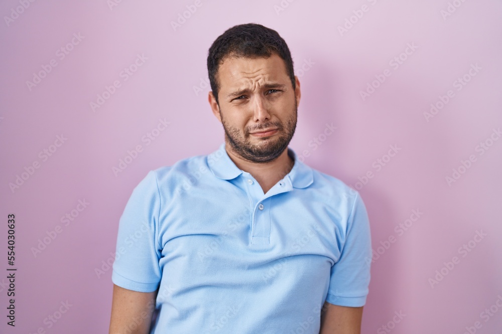Hispanic man standing over pink background depressed and worry for distress, crying angry and afraid. sad expression. Hispanic man standing over pink background depressed and worry for distress, crying angry and afraid. sad expression.
