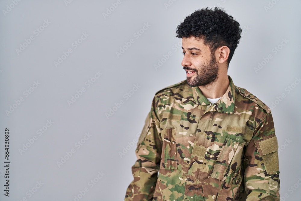 Arab man wearing camouflage army uniform looking away to side with smile on face, natural expression. laughing confident.