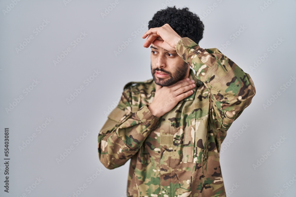 Arab man wearing camouflage army uniform touching forehead for illness and fever, flu and cold, virus sick
