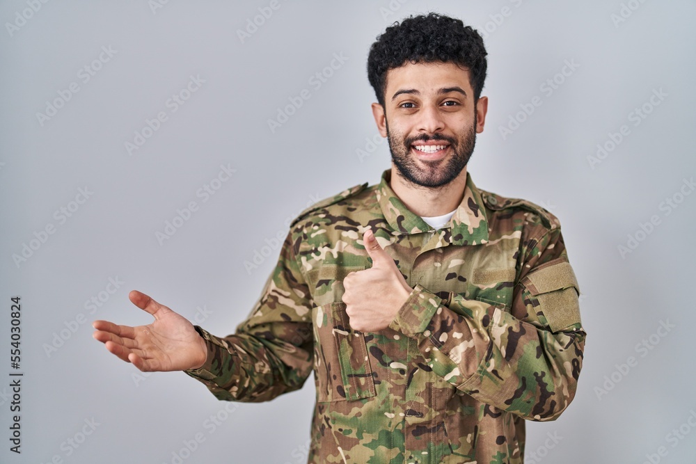 Arab man wearing camouflage army uniform showing palm hand and doing ok gesture with thumbs up, smiling happy and cheerful Arab man wearing camouflage army uniform showing palm hand and doing ok gesture with thumbs up, smiling happy and cheerful