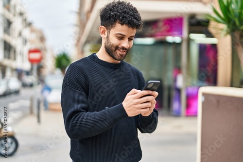 Fotografia Young arab man smiling confident using smartphone at street