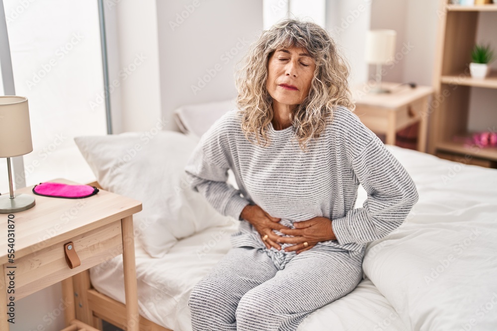 Middle age woman suffering for menstrual pain sitting on bed at bedroom Middle age woman suffering for menstrual pain sitting on bed at bedroom
