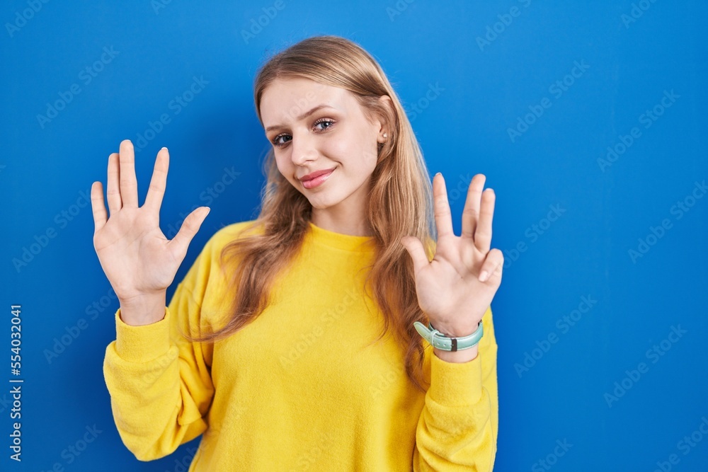 Fototapeta premium Young caucasian woman standing over blue background showing and pointing up with fingers number nine while smiling confident and happy.