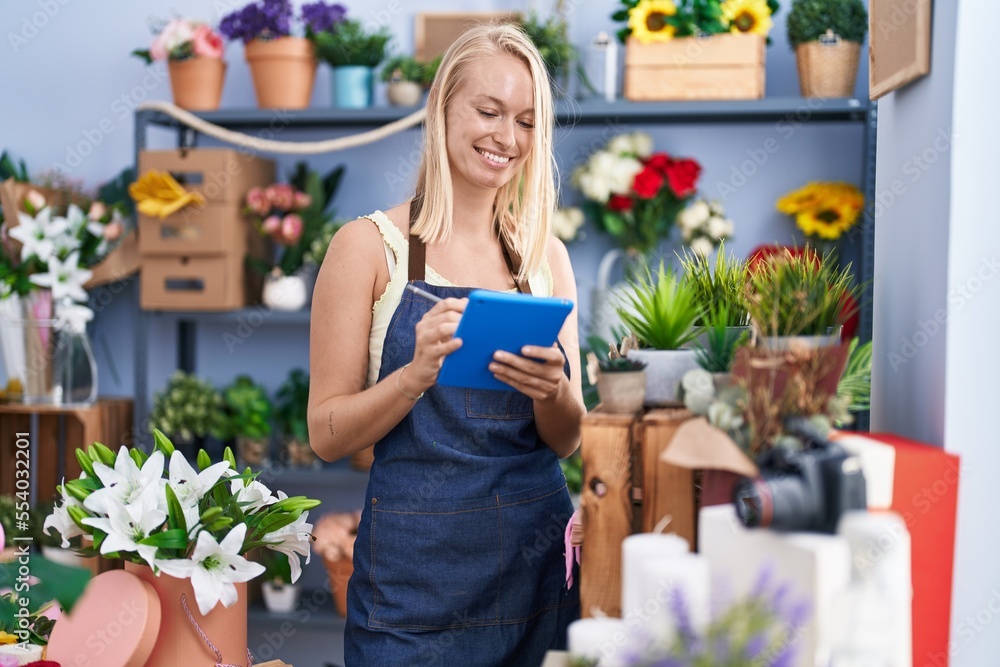 Young blonde woman florist smiling confident writing on touchpad at florist store