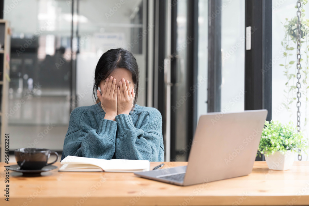 Young woman looks stressed, sitting at the desk, using a laptop, thinking and looking at the camera, feeling tired and bored with depression problems Young woman looks stressed, sitting at the desk, using a laptop, thinking and looking at the camera, feeling tired and bored with depression problems