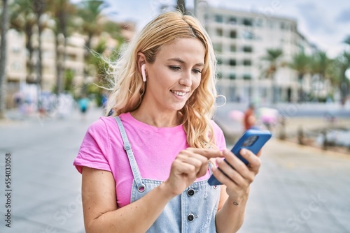 Young blonde woman smiling confident using smartphone at seaside