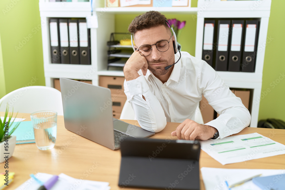 Young hispanic man call center agent working tired sleeping at office Young hispanic man call center agent working tired sleeping at office