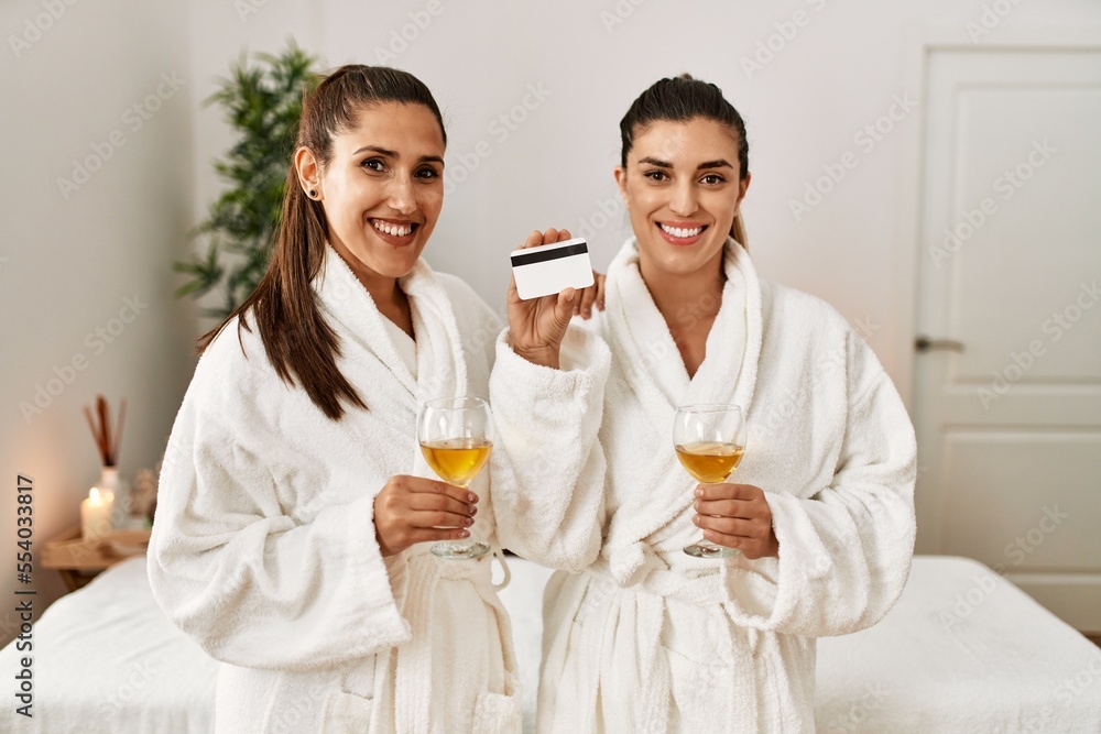 Two women holding credit card toasting with champagne standing at beauty center Two women holding credit card toasting with champagne standing at beauty center