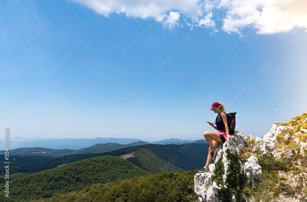 explorer woman sitting looking her smartphone with in background a mountain panoramic view