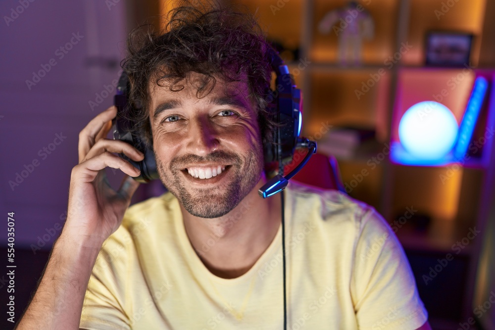 Young hispanic man streamer smiling confident sitting on table at gaming room Young hispanic man streamer smiling confident sitting on table at gaming room