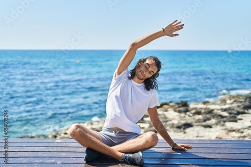 Fototapeta Naklejka Na Ścianę i Meble -  Young hispanic man doing yoga exercise sitting on bench at seaside