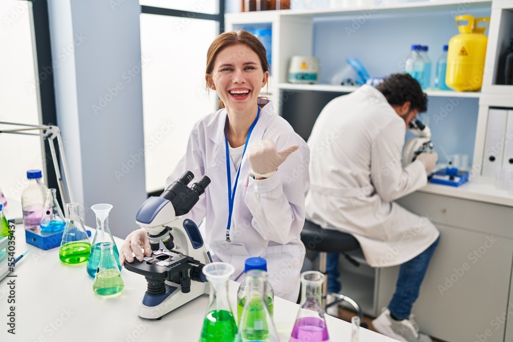 Young two people working at scientist laboratory pointing thumb up to the side smiling happy with open mouth Young two people working at scientist laboratory pointing thumb up to the side smiling happy with open mouth
