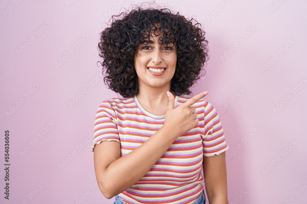 Young middle east woman standing over pink background cheerful with a smile on face pointing with hand and finger up to the side with happy and natural expression Young middle east woman standing over pink background cheerful with a smile on face pointing with hand and finger up to the side with happy and natural expression