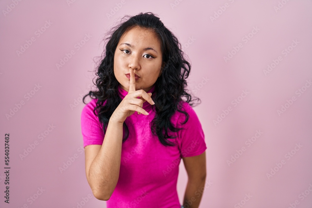 Young asian woman standing over pink background asking to be quiet with finger on lips. silence and secret concept. Young asian woman standing over pink background asking to be quiet with finger on lips. silence and secret concept.