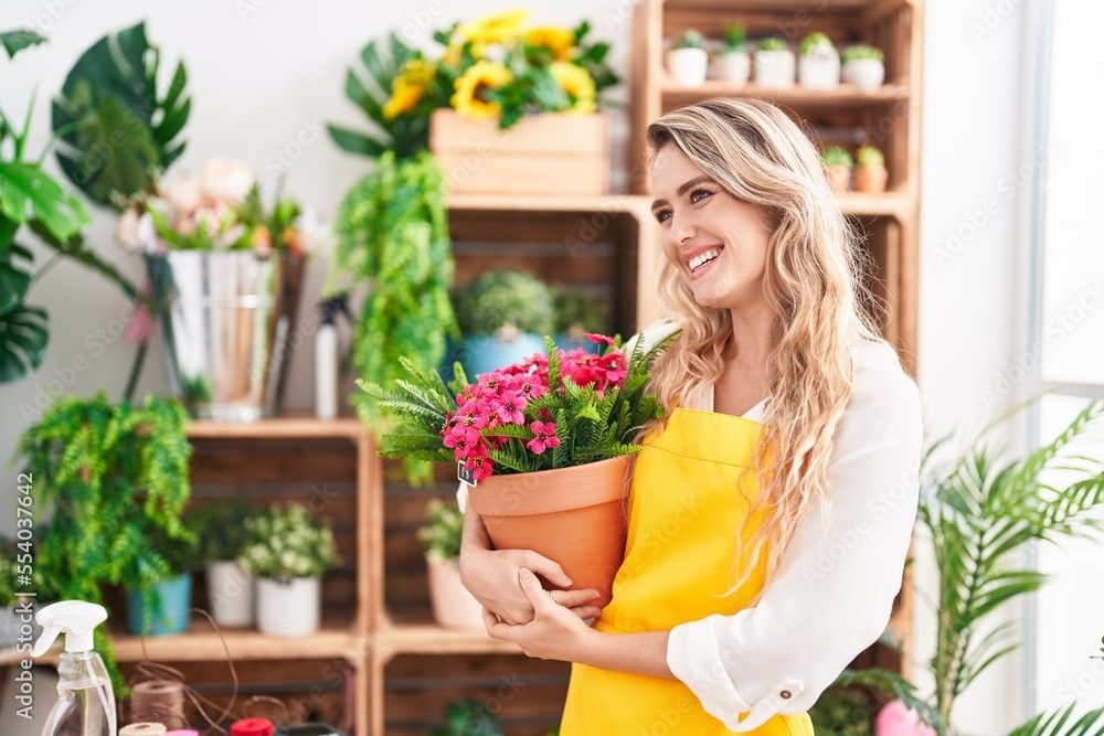 Young blonde woman florist smiling confident holding plant at florist Young blonde woman florist smiling confident holding plant at florist