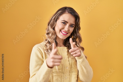 Young caucasian woman standing over yellow background pointing fingers to camera with happy and funny face. good energy and vibes.