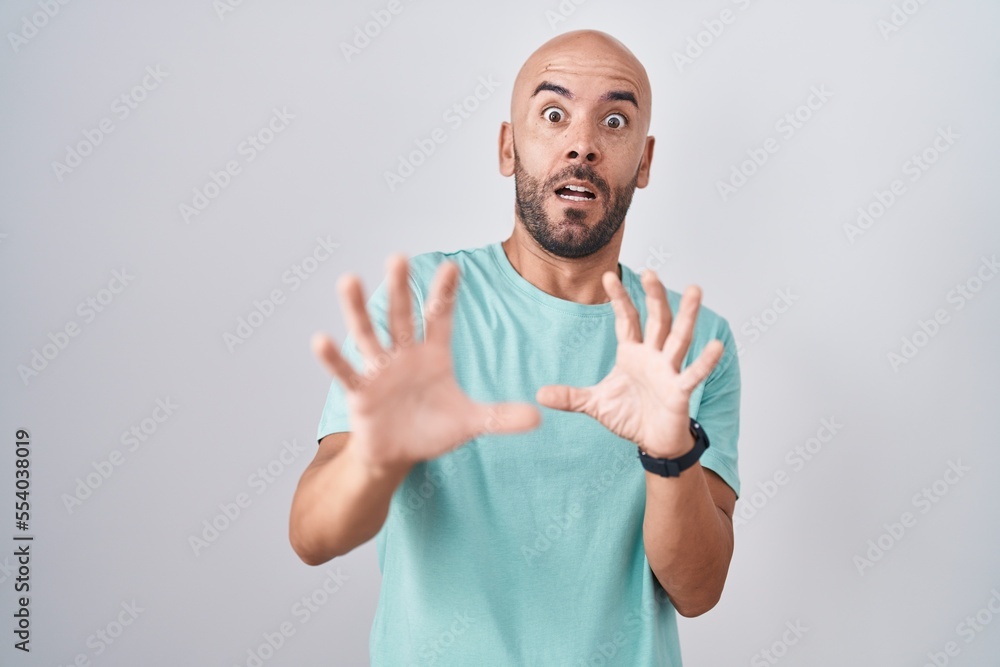 Naklejka premium Middle age bald man standing over white background afraid and terrified with fear expression stop gesture with hands, shouting in shock. panic concept.