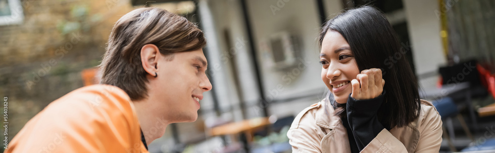 Positive asian woman in trench coat talking to boyfriend in outdoor cafe, banner. Positive asian woman in trench coat talking to boyfriend in outdoor cafe, banner.