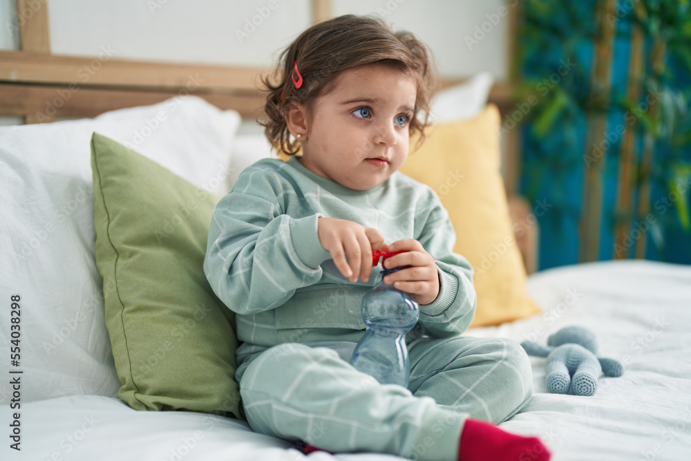 Adorable hispanic girl sitting on bed with holding water bottle at bedroom