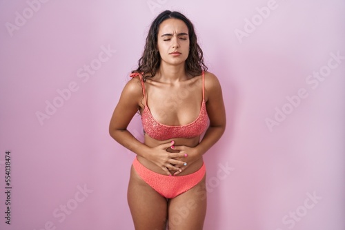 Young hispanic woman wearing lingerie over pink background with hand on stomach because indigestion, painful illness feeling unwell. ache concept.