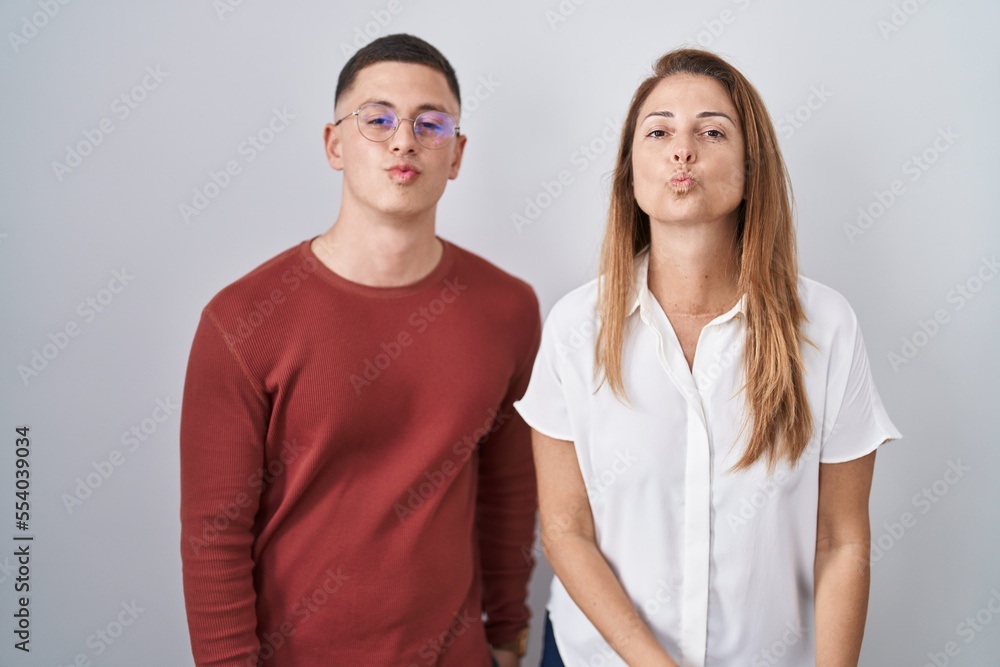 Mother and son standing together over isolated background looking at the camera blowing a kiss on air being lovely and sexy. love expression. Mother and son standing together over isolated background looking at the camera blowing a kiss on air being lovely and sexy. love expression.