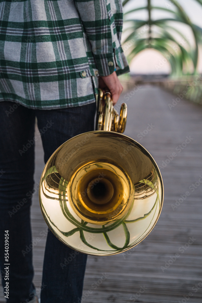 Musician walking on a bridge with his horn in his hand.