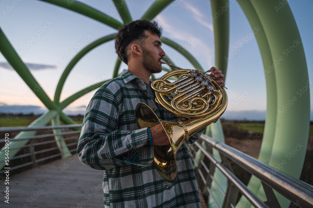 Musician walking on a bridge with his horn in his hand.