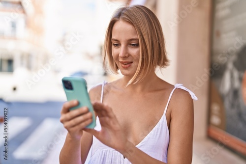 Young blonde woman smiling confident using smartphone at street