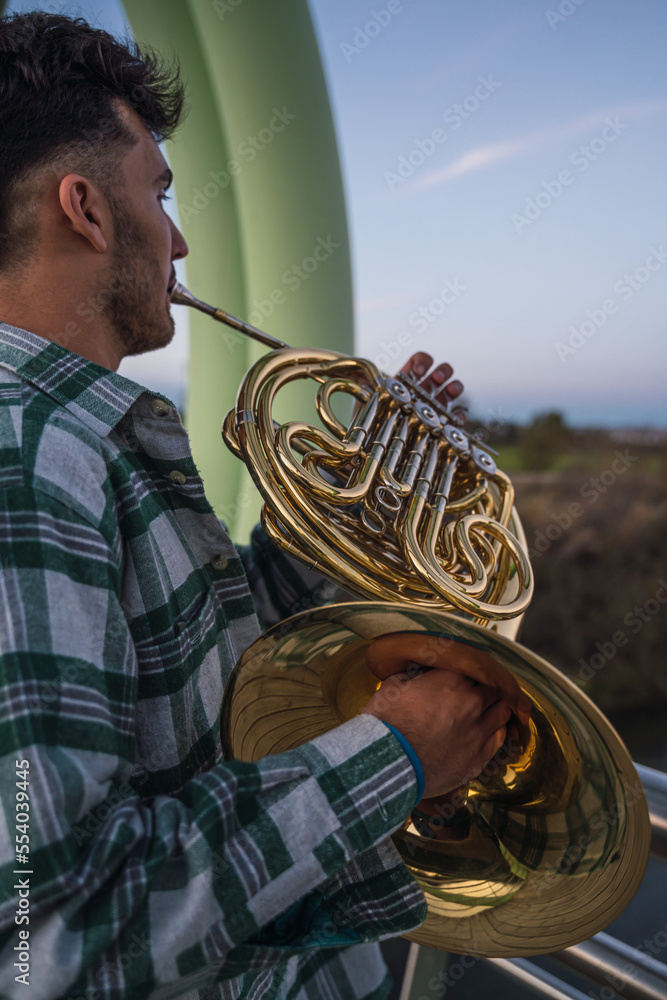 Musician walking on a bridge with his horn in his hand.