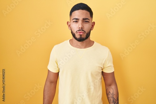 Young hispanic man standing over yellow background looking at the camera blowing a kiss on air being lovely and sexy. love expression.