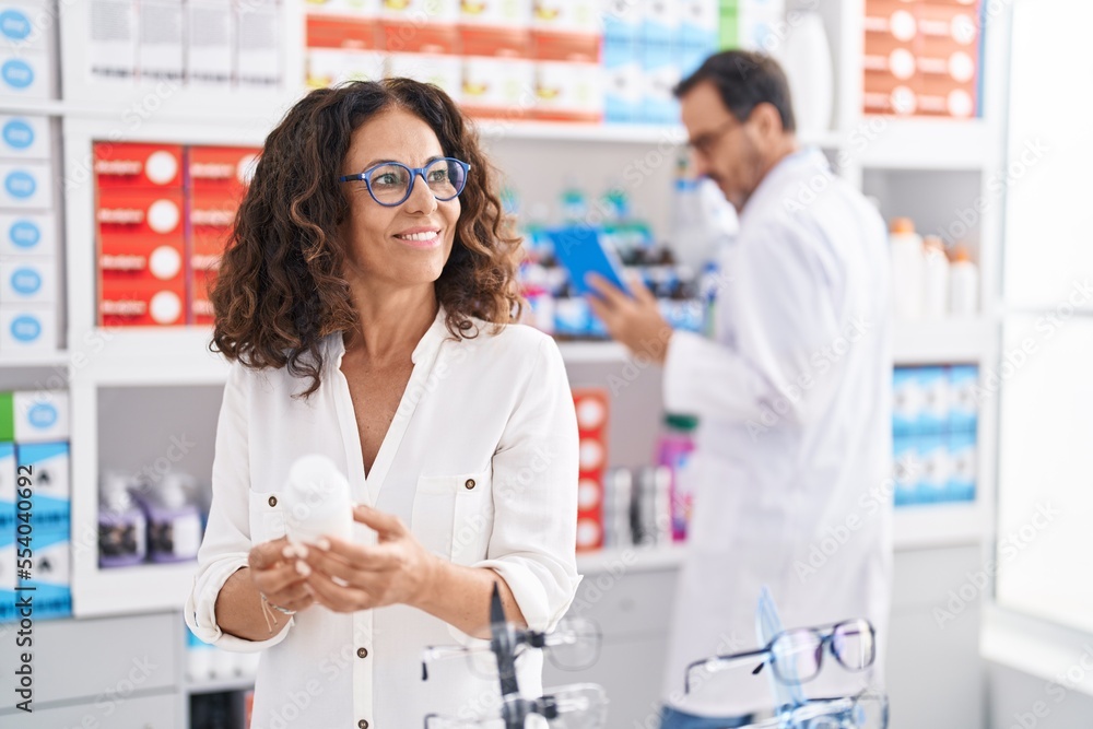 Fototapeta premium Man and woman pharmacists using touchpad and client holding pills bottle at pharmacy