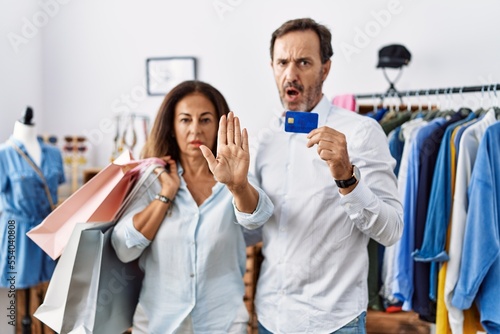 Hispanic middle age couple holding shopping bags and credit card doing stop gesture with hands palms  angry and frustration expression