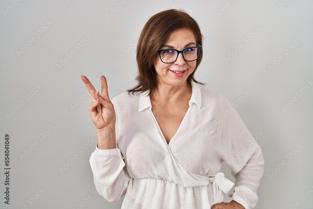Middle age hispanic woman standing over isolated background smiling with happy face winking at the camera doing victory sign. number two. Middle age hispanic woman standing over isolated background smiling with happy face winking at the camera doing victory sign. number two.