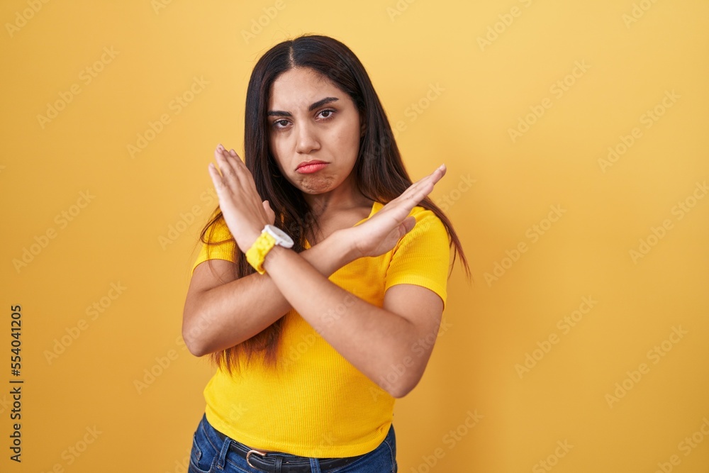 Young arab woman standing over yellow background rejection expression crossing arms doing negative sign, angry face Young arab woman standing over yellow background rejection expression crossing arms doing negative sign, angry face