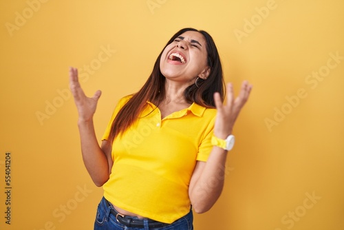 Young arab woman standing over yellow background celebrating mad and crazy for success with arms raised and closed eyes screaming excited. winner concept