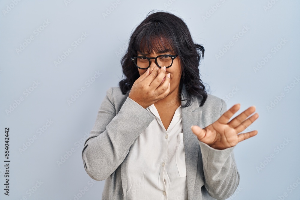 Hispanic woman standing over isolated background smelling something stinky and disgusting, intolerable smell, holding breath with fingers on nose. bad smell Hispanic woman standing over isolated background smelling something stinky and disgusting, intolerable smell, holding breath with fingers on nose. bad smell