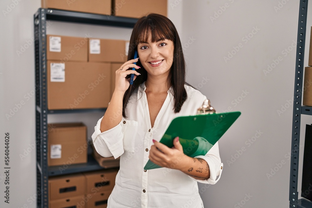 Young beautiful hispanic woman ecommerce business worker holding clipboard talking on smartphone at office Young beautiful hispanic woman ecommerce business worker holding clipboard talking on smartphone at office