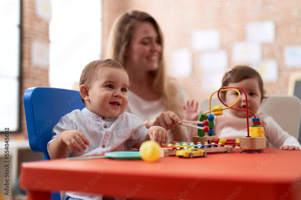 Teacher and preschool students playing with toys sitting on table at kindergarten Teacher and preschool students playing with toys sitting on table at kindergarten