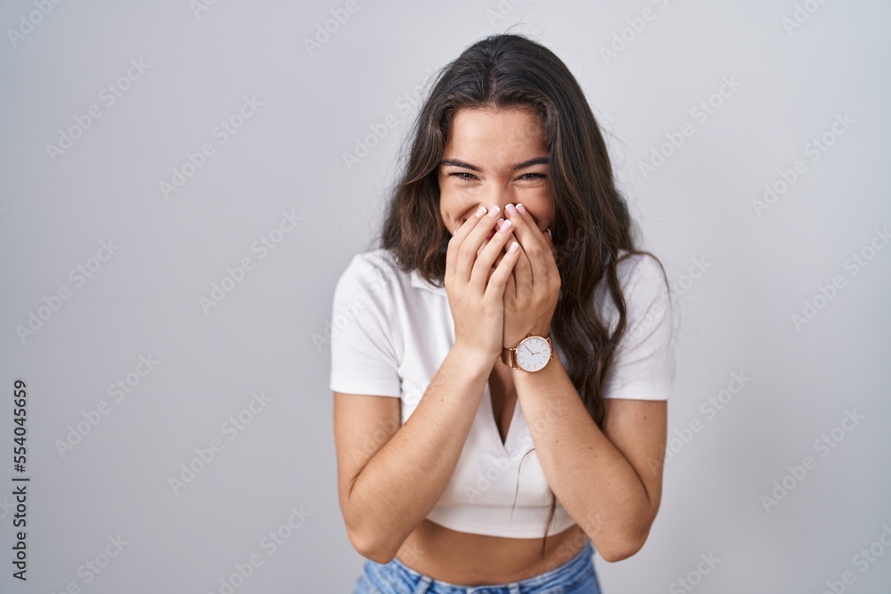 Young teenager girl standing over white background laughing and embarrassed giggle covering mouth with hands, gossip and scandal concept Young teenager girl standing over white background laughing and embarrassed giggle covering mouth with hands, gossip and scandal concept