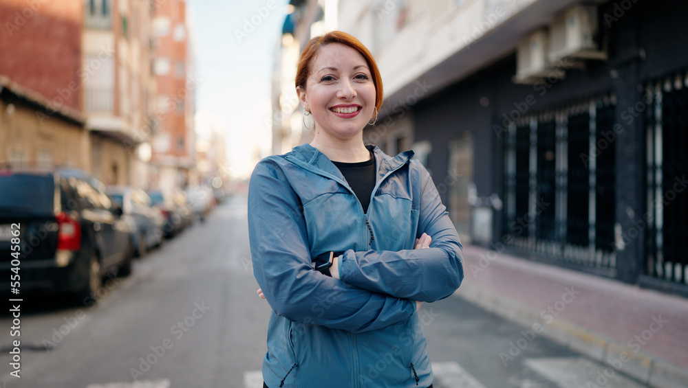 Fototapeta premium Young redhead woman wearing sportswear standing with arms crossed gesture at street